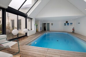Una piscina interior con terraza de madera, ventanas amplias y vistas al exterior.