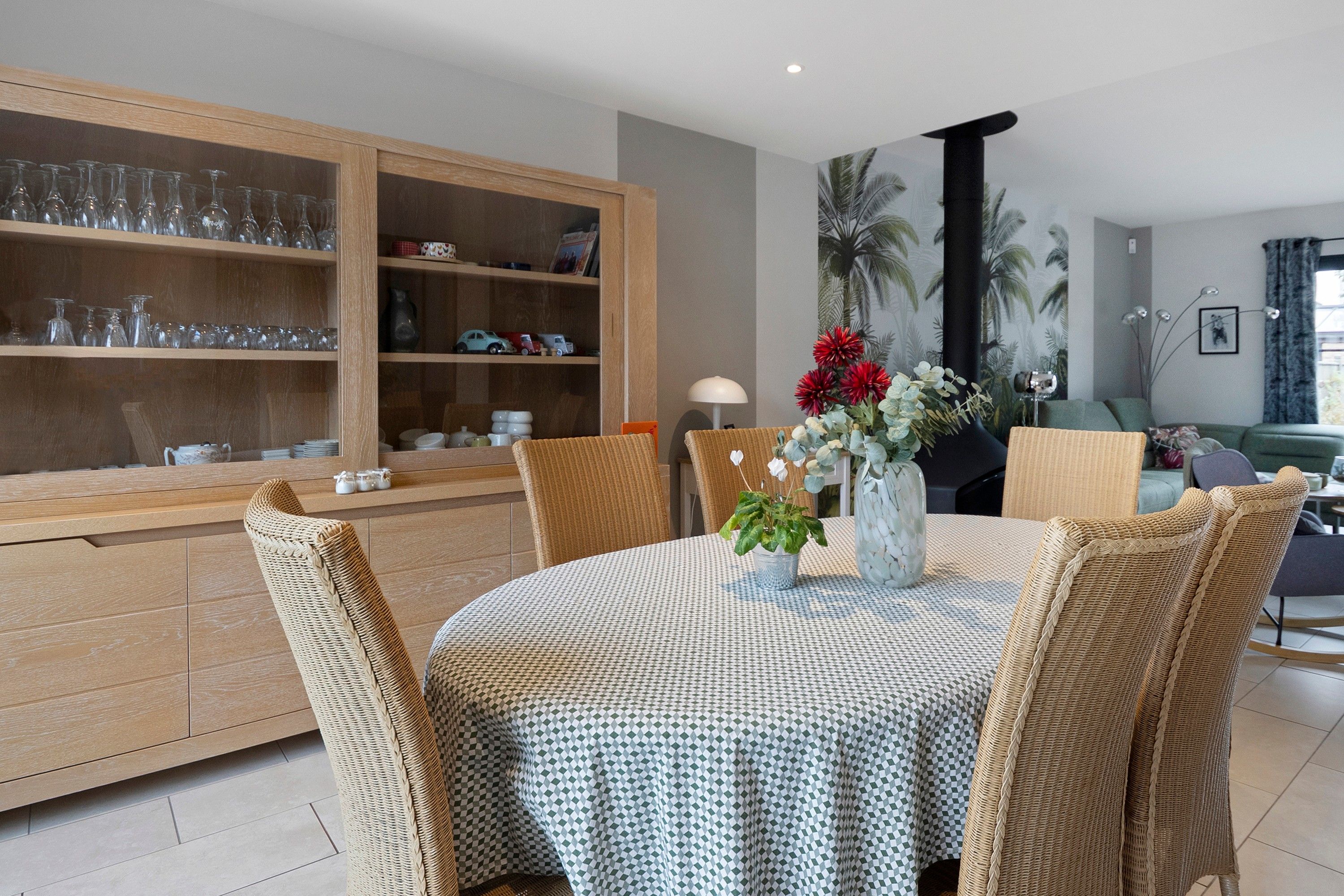 Un coin repas avec une nappe à carreaux, des chaises en osier et un buffet en bois contenant de la verrerie.