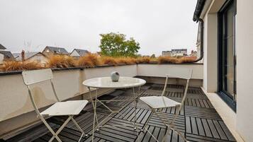 Une terrasse sur le toit, avec une table ronde et quatre chaises, un pot de fleurs et une vue sur les bâtiments voisins.