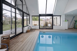 A modern indoor swimming pool with a wooden deck, large windows, and a view of the surrounding area. - Bed and Breakfast 'Chambre Black and White' with Shared Terrace, Balcony and Wi-Fi (Caen)