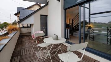 Un patio exterior con mesa y sillas, una planta en maceta y vistas del interior a través de una puerta de cristal.