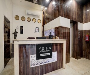 A reception desk with a sign indicating it's company-serviced, surrounded by wooden paneling, a clock, and a fire extinguisher. - Classic Hotel Metro View (Jaipur)