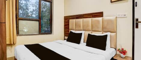 A bedroom with a large window, a bed with white and black bedding, a wooden headboard, and a small bedside table with a vase of flowers.