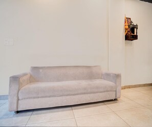 A light-colored sofa in a room with a tiled floor and a plain white wall. - Classic Hotel Metro View (Jaipur)