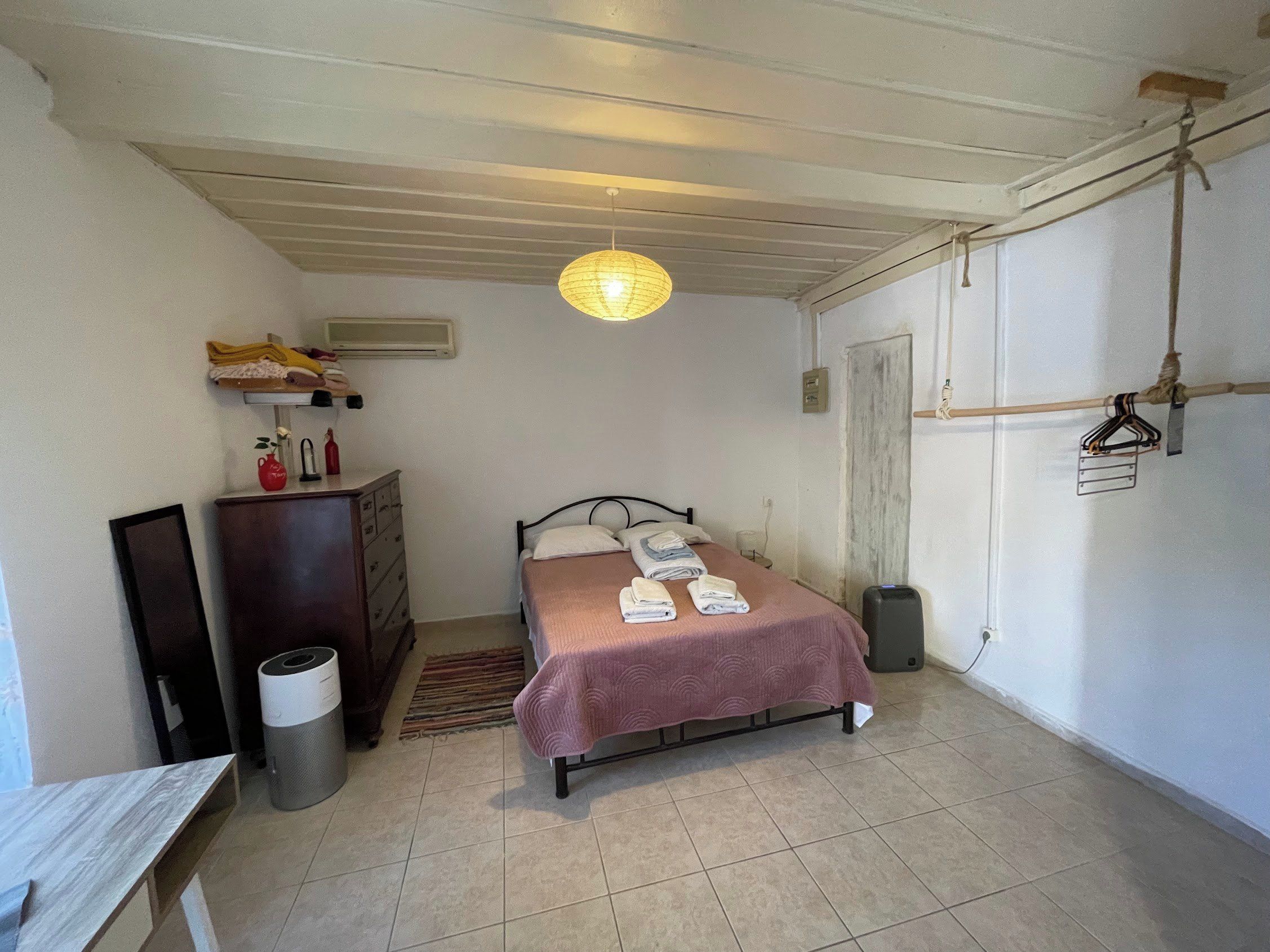 A bedroom with a bed, a dresser, a hanging light fixture, and a door.