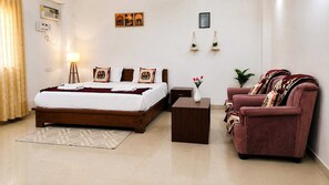 Ein Hotelzimmer mit Bett, Nachttisch, Sessel und einem kleinen Tisch mit Blumenvase.