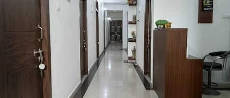 A hotel corridor with wooden doors, a reception desk, and a chair.