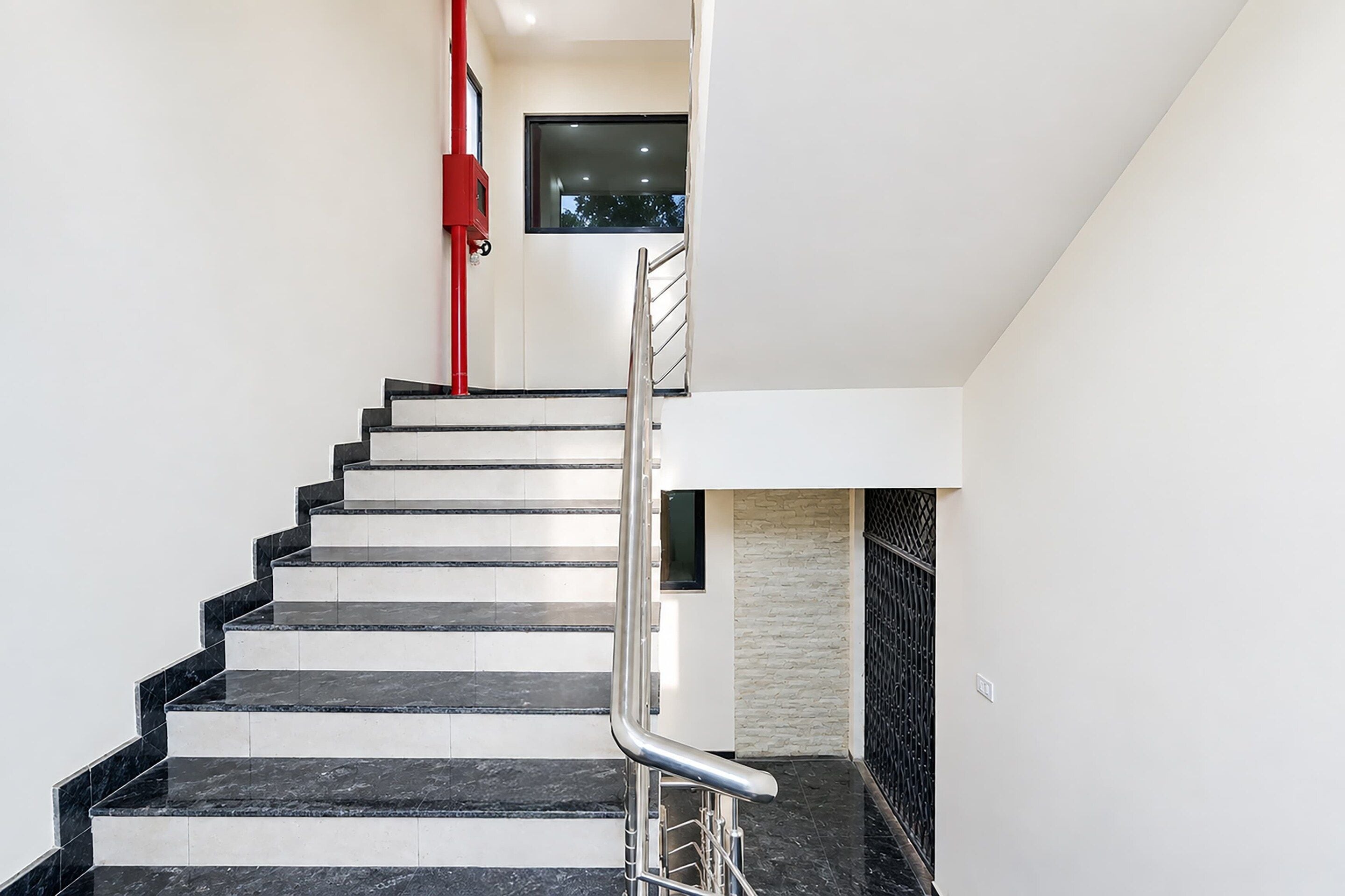 A modern staircase with a metal handrail, leading to a landing with a small window.