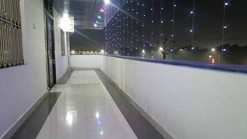 A corridor with a tiled floor, a railing, and string lights.
