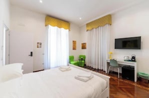 A hotel room with a bed, a desk, a chair, a television, and a window with curtains. - Marina Rooms (Napoli)