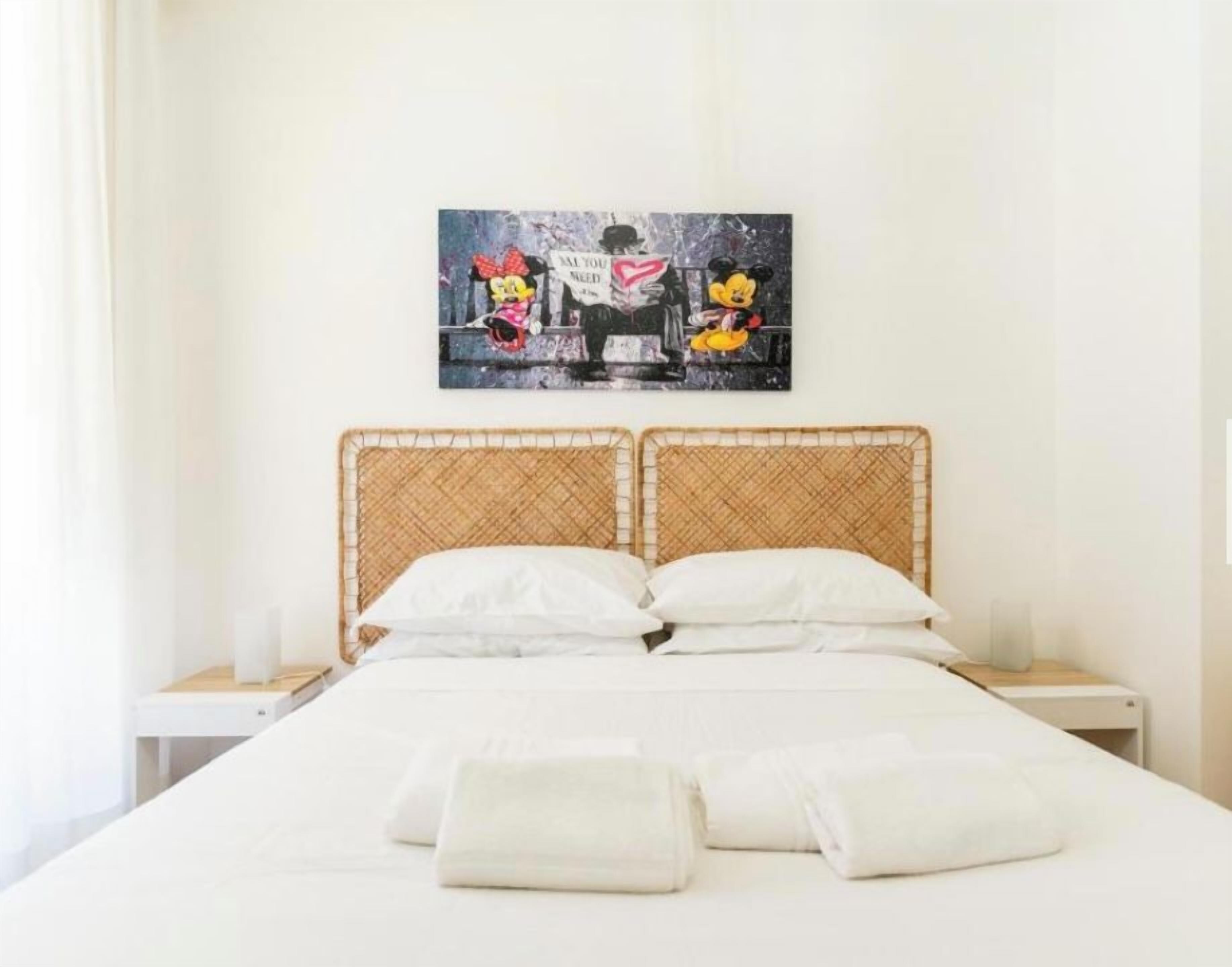 A hotel room with a bed, two nightstands, a wall-mounted artwork, and a window with curtains.