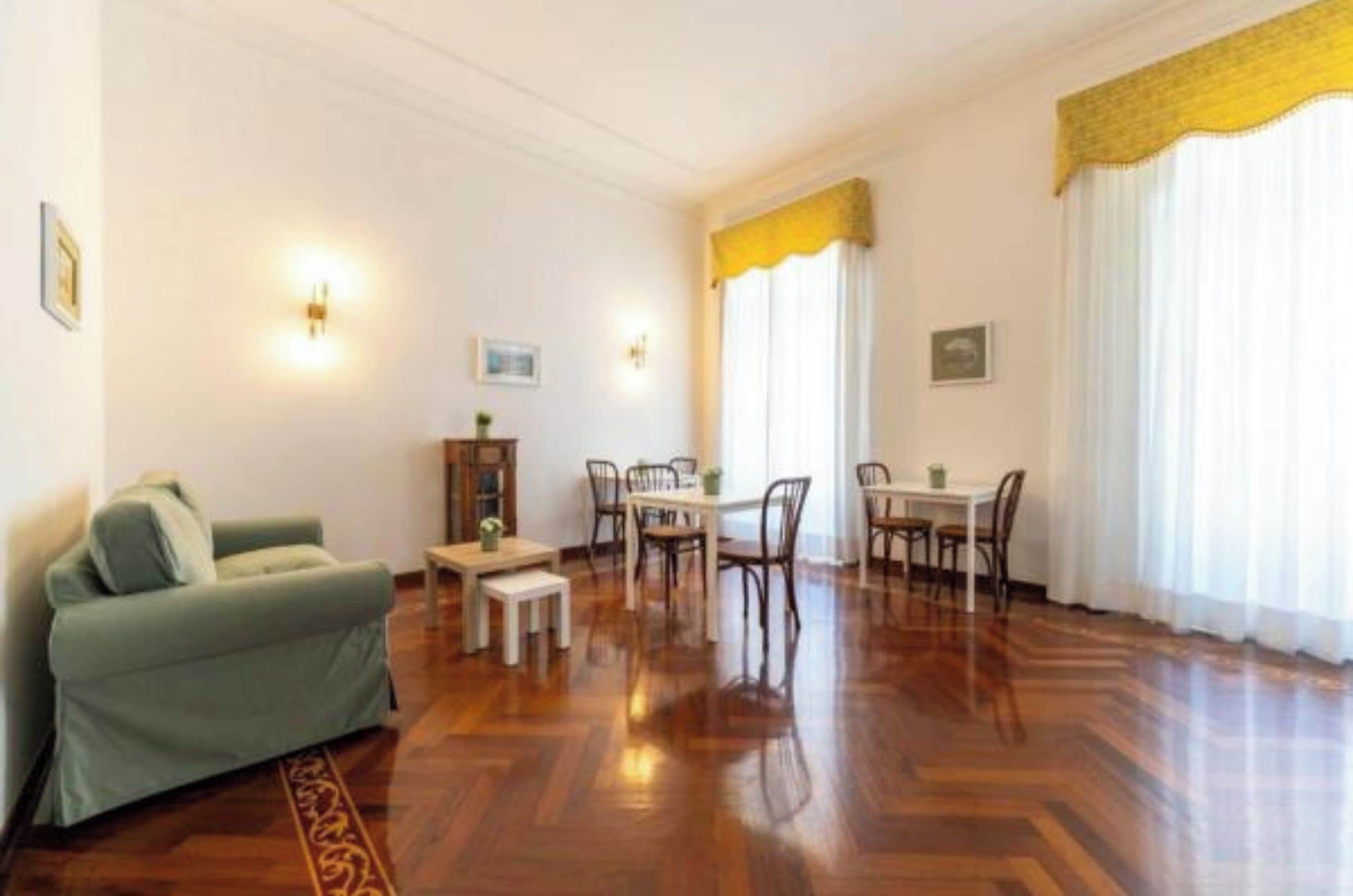 Una stanza con un divano, un tavolo da pranzo con sedie e una finestra con tende.