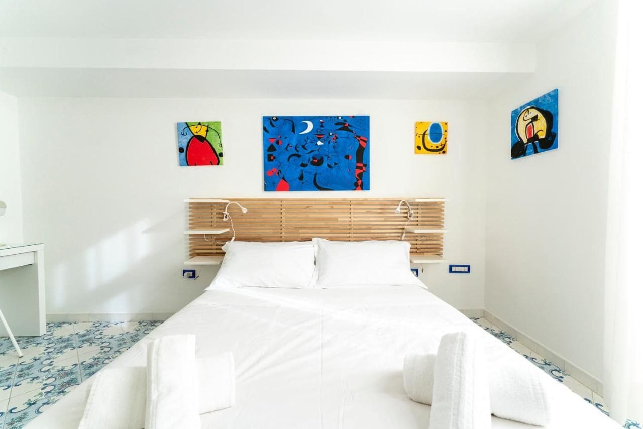 Ett hotellrum med en säng, vita sängkläder, en träpanel som huvudgavel och fyra konstverk på väggarna.