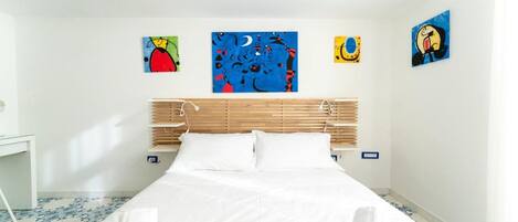 Ett hotellrum med en säng, vita sängkläder, en träpanel som huvudgavel och fyra konstverk på väggarna.
