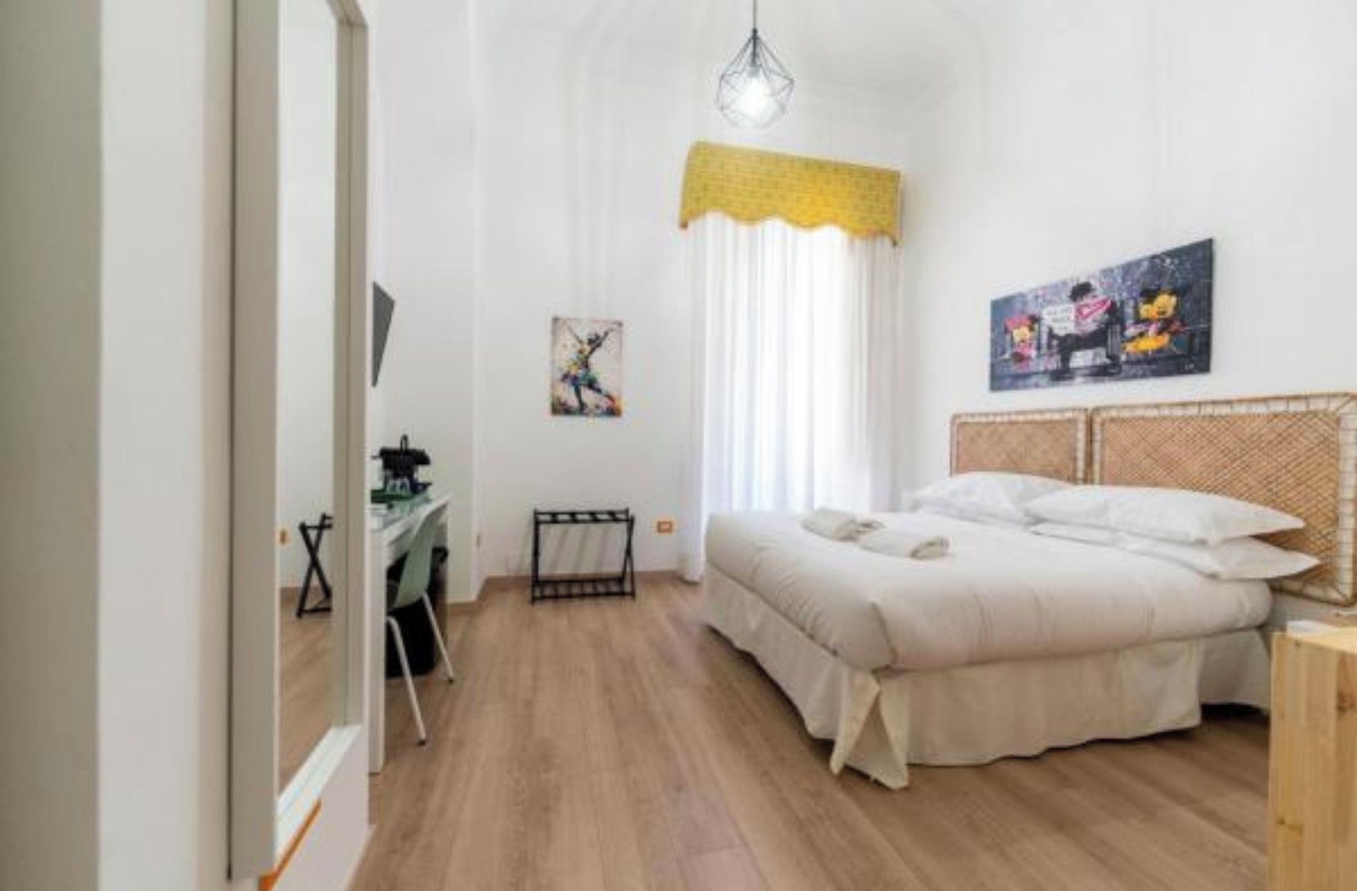 A bedroom with a bed, a desk, and a chair. There is a window with curtains and a painting on the wall.