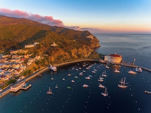 A coastal town with a marina filled with boats, a prominent building with a red roof, and a bridge connecting the town to the mainland. - Seaport Village Inn, Avalon | 2 Ocean View Suites | 1 Queen Bed (Avalon)