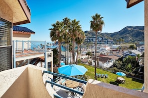 A balcony with a view of a coastal town, palm trees, and a mountain in the background. - Seaport Village Inn, Avalon | 2 Ocean View Suites | 1 Queen Bed (Avalon)