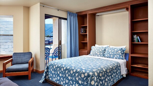 Une chambre avec un lit, une chaise, une bibliothèque et une vue sur l’extérieur, accessible par une porte coulissante.