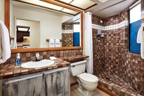 Ein Badezimmer mit gefliestem Duschbereich, Waschbecken mit Spiegel und Toilette.