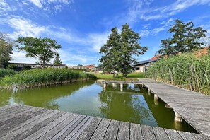 A wooden dock extending over a calm water body with a grassy area and trees in the background. - Holiday apartment with private lake access and jetty (Klein Labenz)