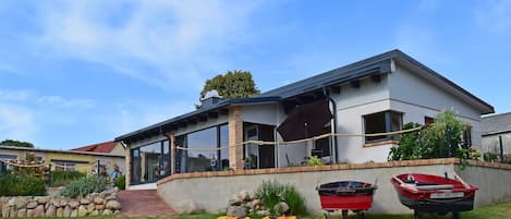 A modern house with a covered porch, a stone wall, and two boats.