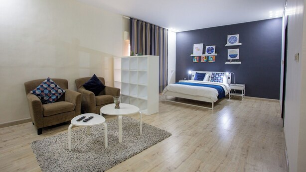 A modern bedroom with a bed, a sofa, a small table, and a bookshelf. - ALBASEM Hotel Apartments (Amman)