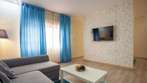 A modern living room with a sofa, a coffee table, and a flat-screen TV mounted on a wall with a patterned design. - ALBASEM Hotel Apartments (Amman)