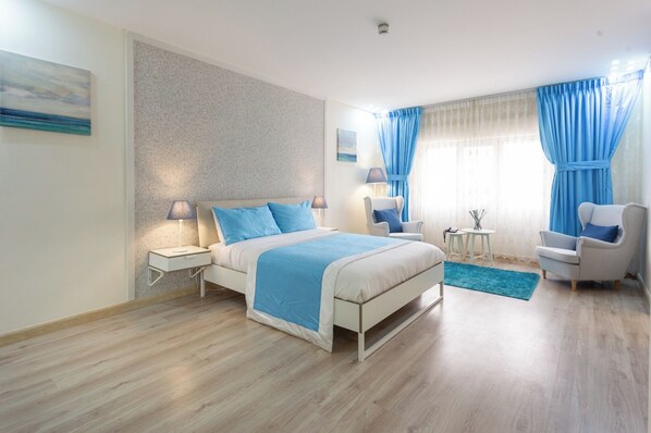 A modern bedroom with a large bed, two bedside tables, a chair, a small table, and a window with curtains.