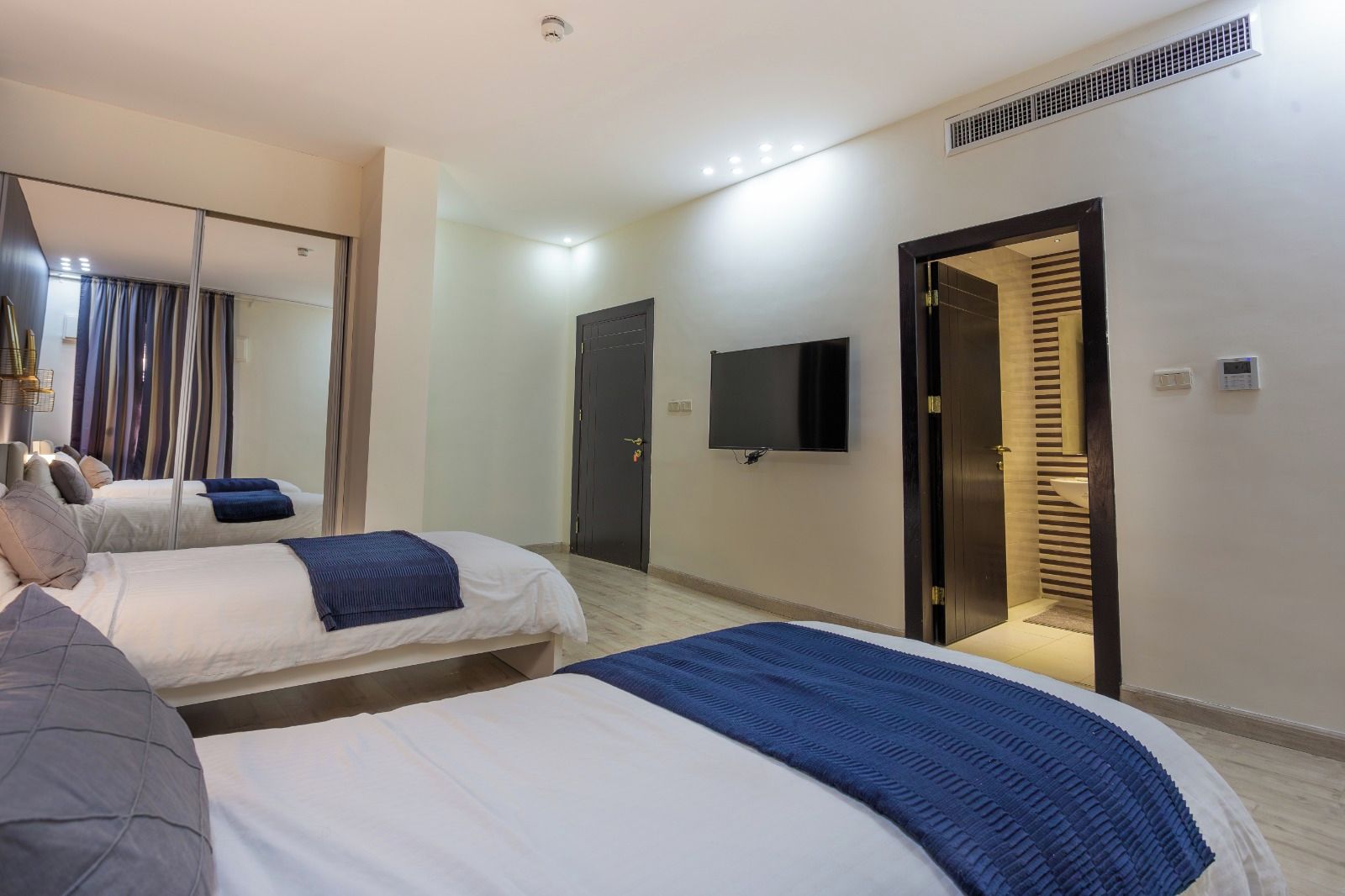 A hotel room with two beds, a flat-screen TV, a mirror, and a door leading to a bathroom.