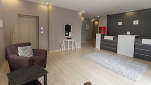 A modern reception area with a reception desk, a seating area with a sofa and a small table, and a mirror on the wall. - ALBASEM Hotel Apartments (Amman)