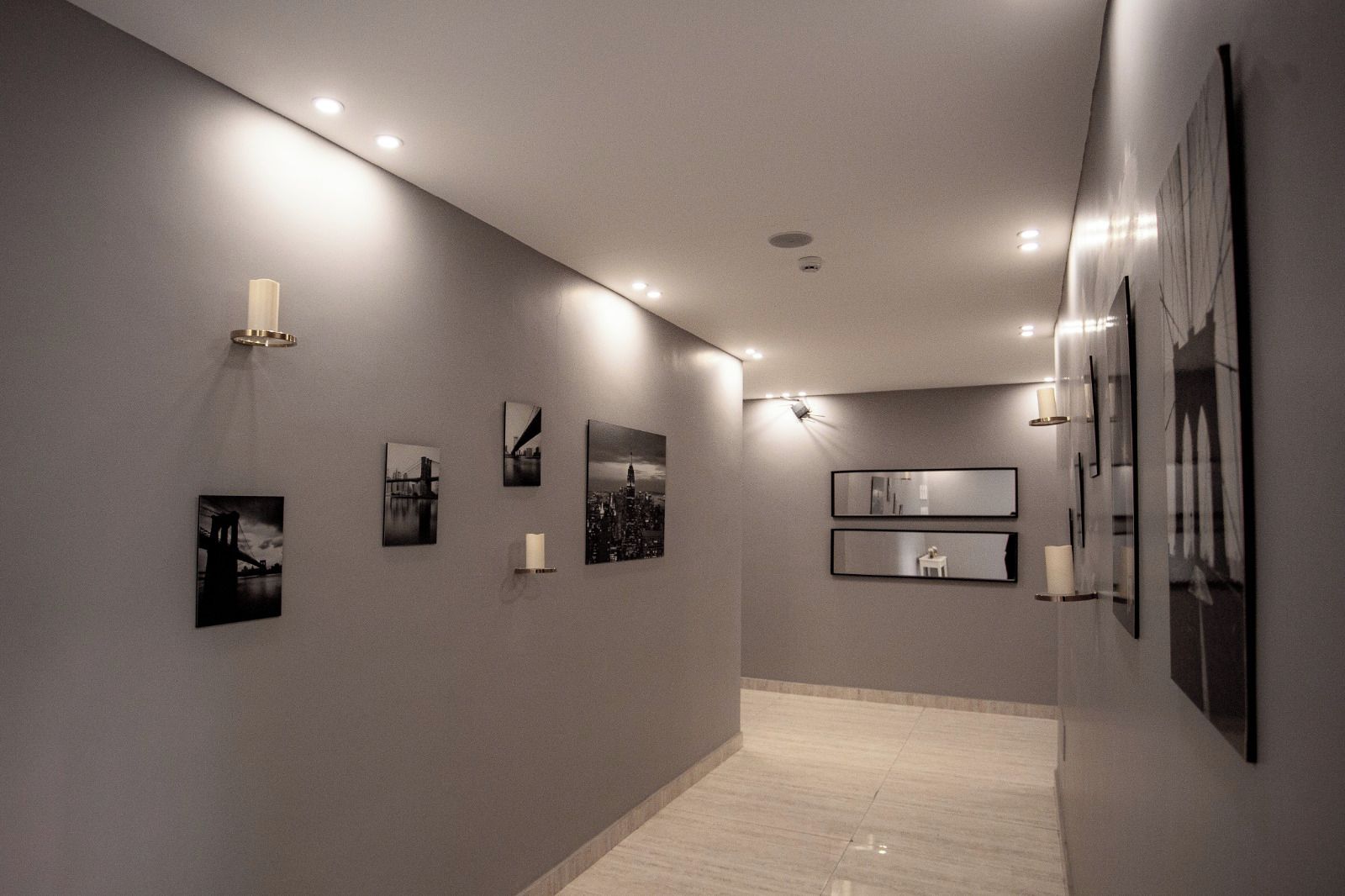Un corridoio con una serie di fotografie incorniciate alle pareti, illuminazione a incasso e pavimento piastrellato.