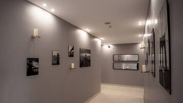 Un corridoio con una serie di fotografie incorniciate alle pareti, illuminazione a incasso e pavimento piastrellato.