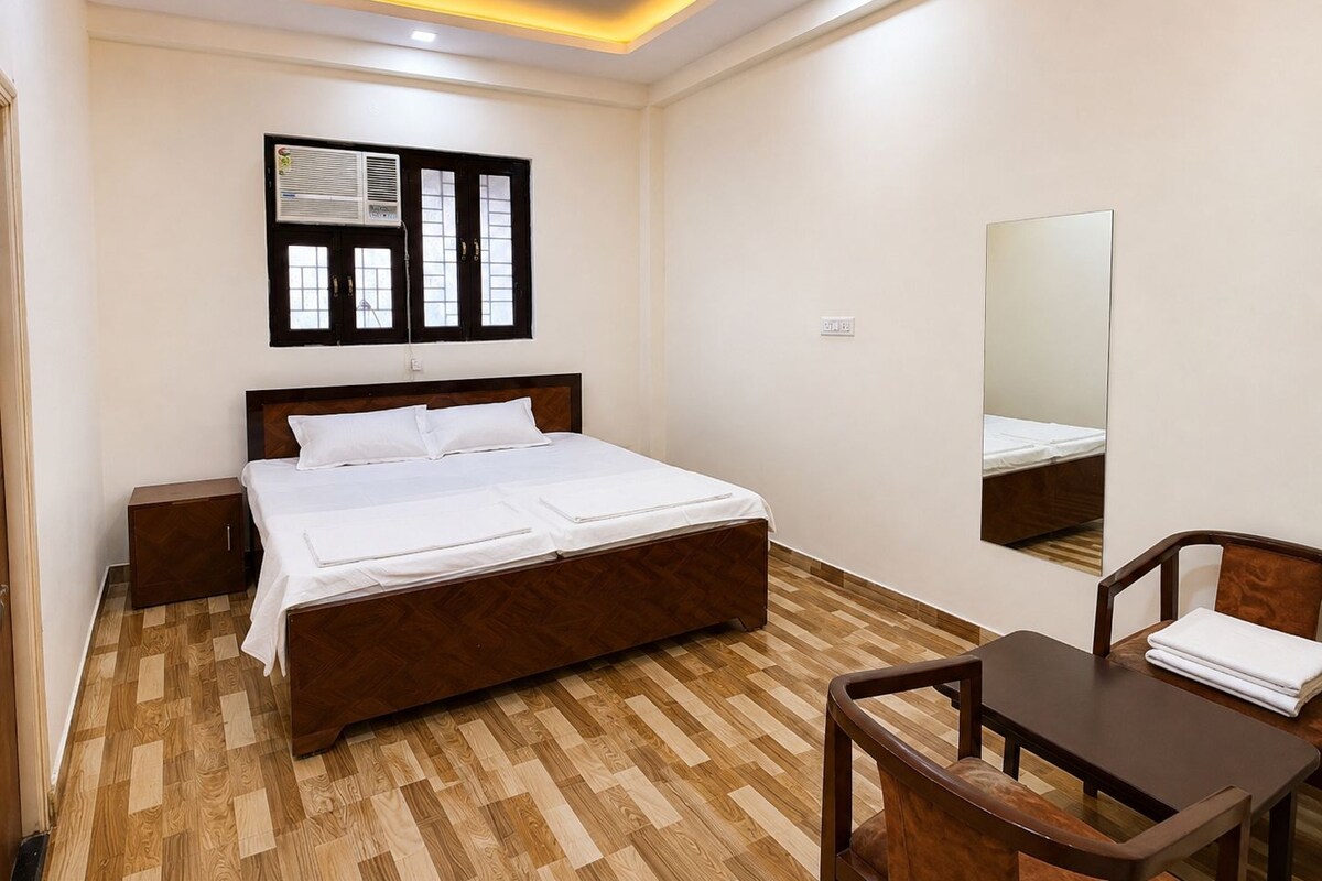 A hotel room with a bed, bedside tables, a desk, a chair, a mirror, and a window with blinds.