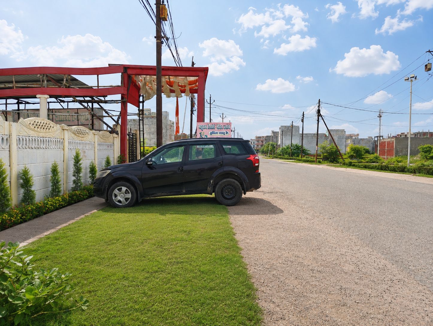 A black SUV parked on a paved road with a grassy area and a red structure in the background.
