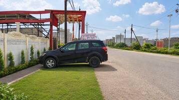 A black SUV parked on a paved road with a grassy area and a red structure in the background.