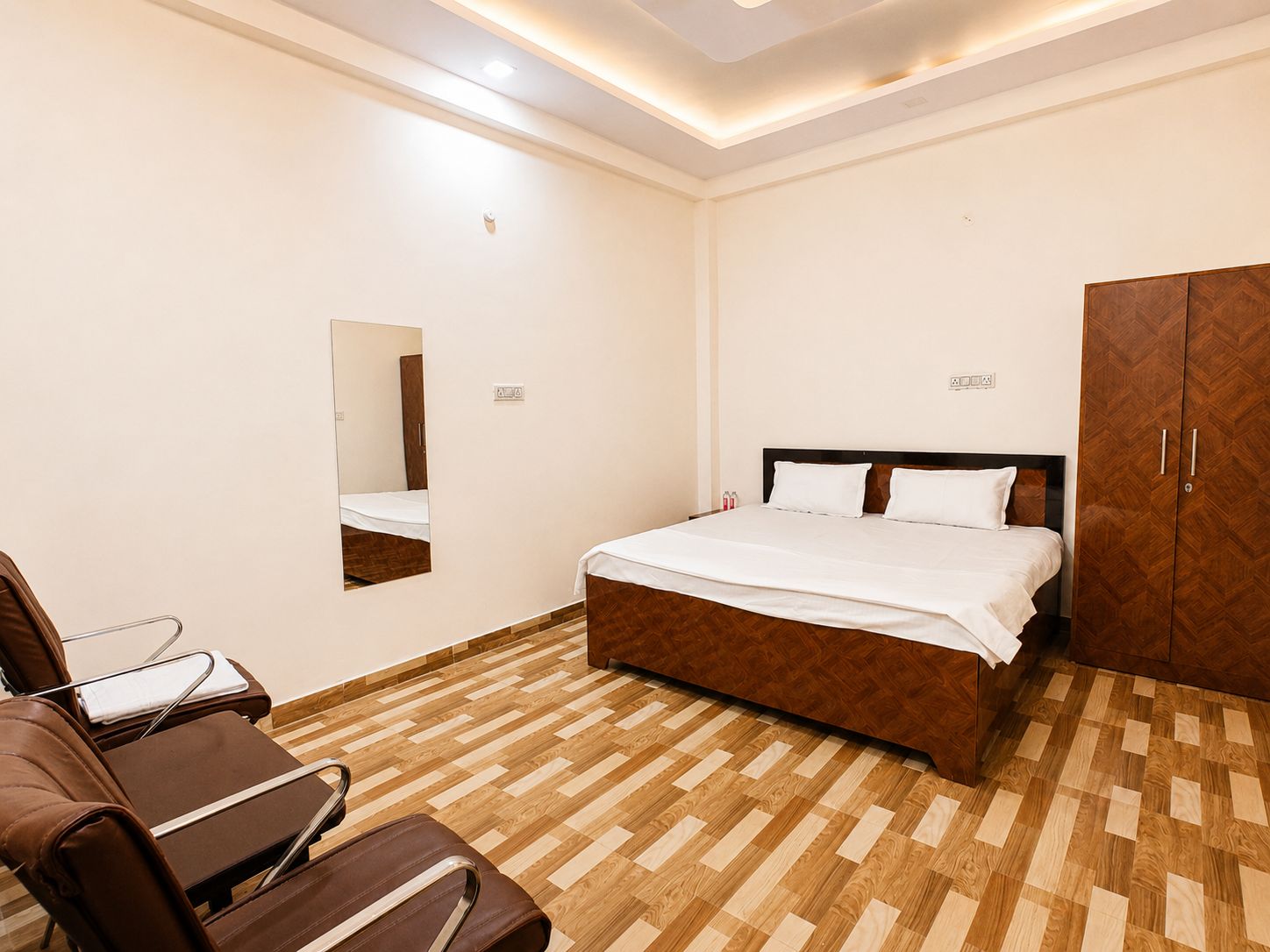 A hotel room with a bed, a mirror, a wardrobe, and a seating area with chairs.