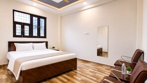 A hotel room with a bed, a chair, a mirror, and a ceiling fan. - Madhuvan Resort (Kanpur)