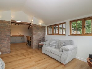 Ein gemütliches Wohnzimmer mit Steinwand, grauem Sofa, Holzboden und einer Küche im Hintergrund.