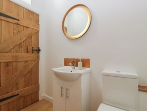 A bathroom with a wooden door, a white sink with a soap dispenser, and a toilet. - Ynys (Abergavenny)