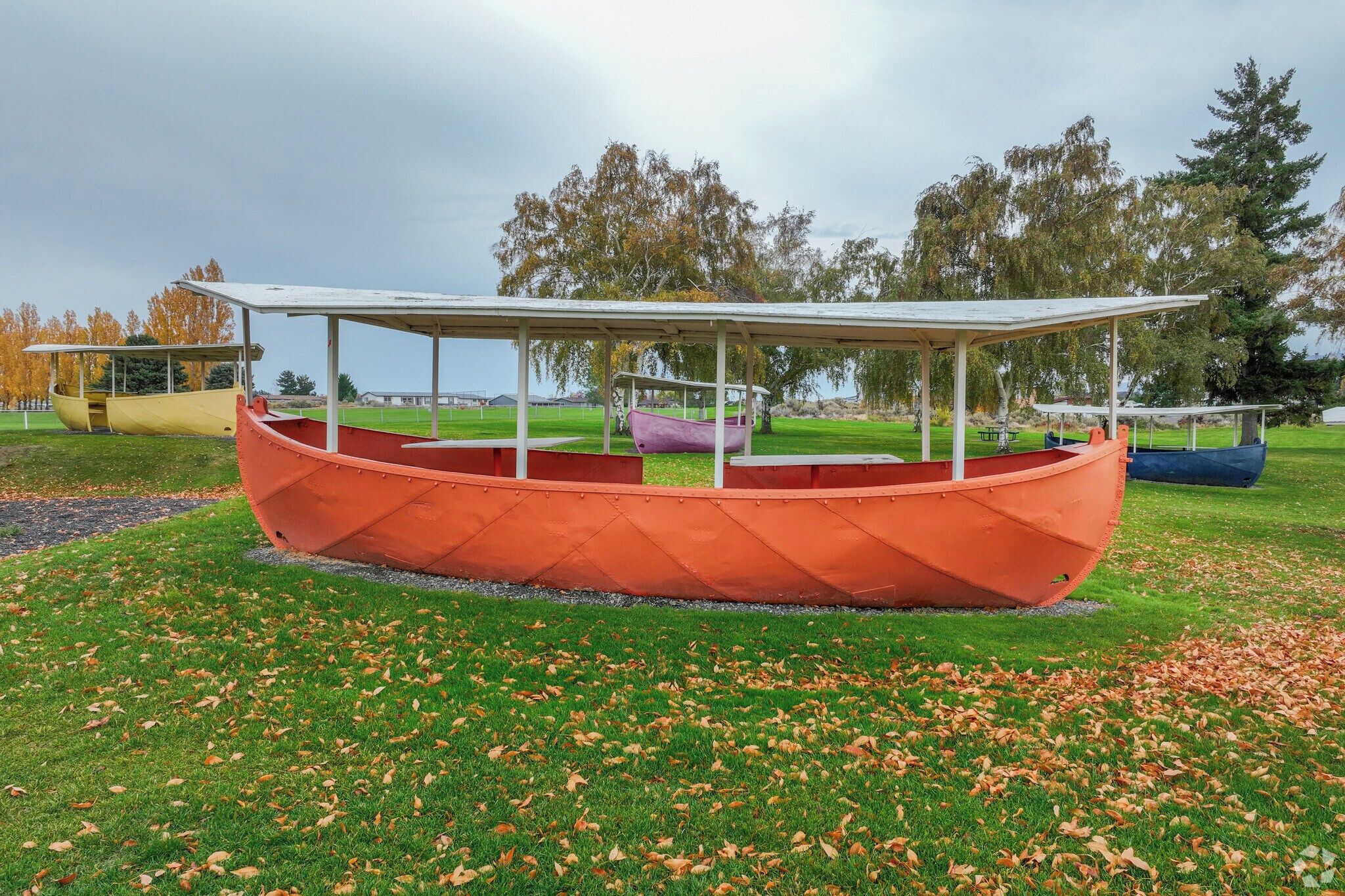 A boat-shaped structure with a roof, surrounded by grass and fallen leaves.