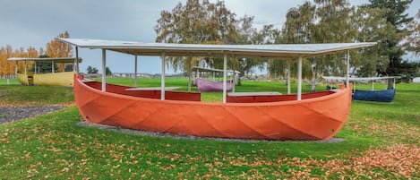 Une structure en forme de bateau, dotée d’un toit et entourée d’herbe et de feuilles mortes.