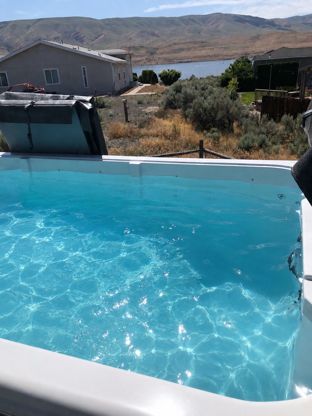 A swimming pool with clear blue water, surrounded by a landscape with hills and a house in the background.