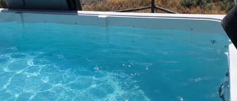 A swimming pool with clear blue water, surrounded by a landscape with hills and a house in the background.