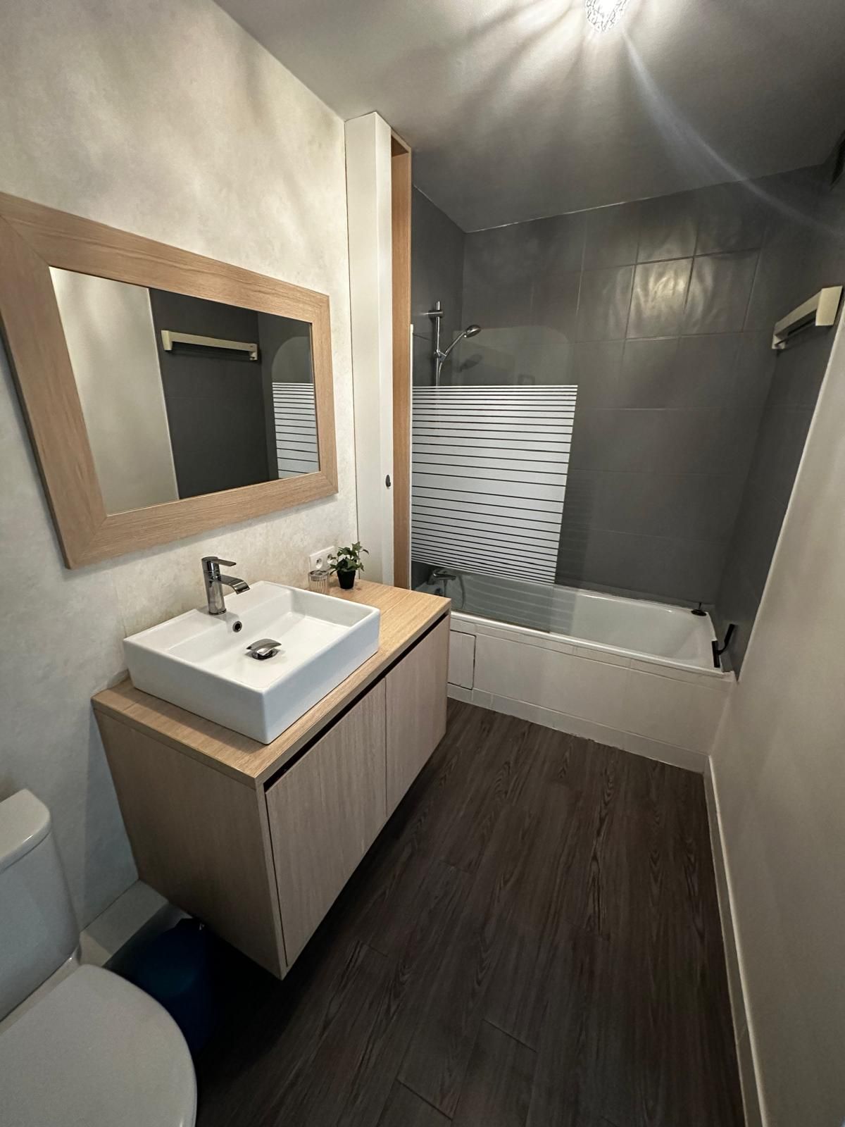 A modern bathroom with a wooden vanity, a white sink, a mirror, a shower, and a bathtub.
