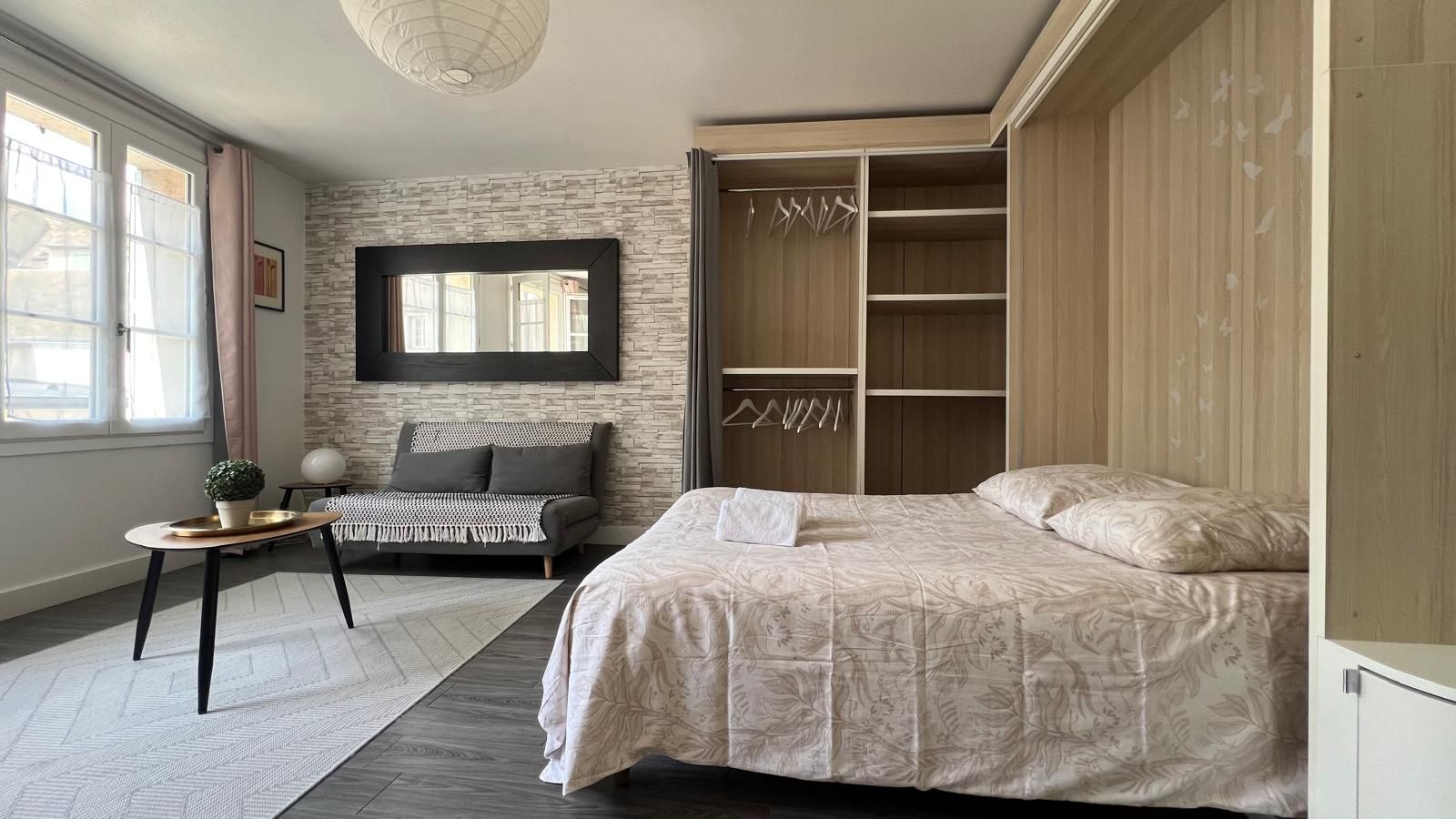 Une chambre à coucher avec un lit, un canapé, une armoire, un miroir et une petite table sur laquelle est posée une plante.