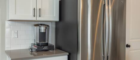 Ein Edelstahl-Kühlschrank mit integriertem Eisbereiter, eine Kaffeemaschine auf der Arbeitsplatte und weiße Schränke.