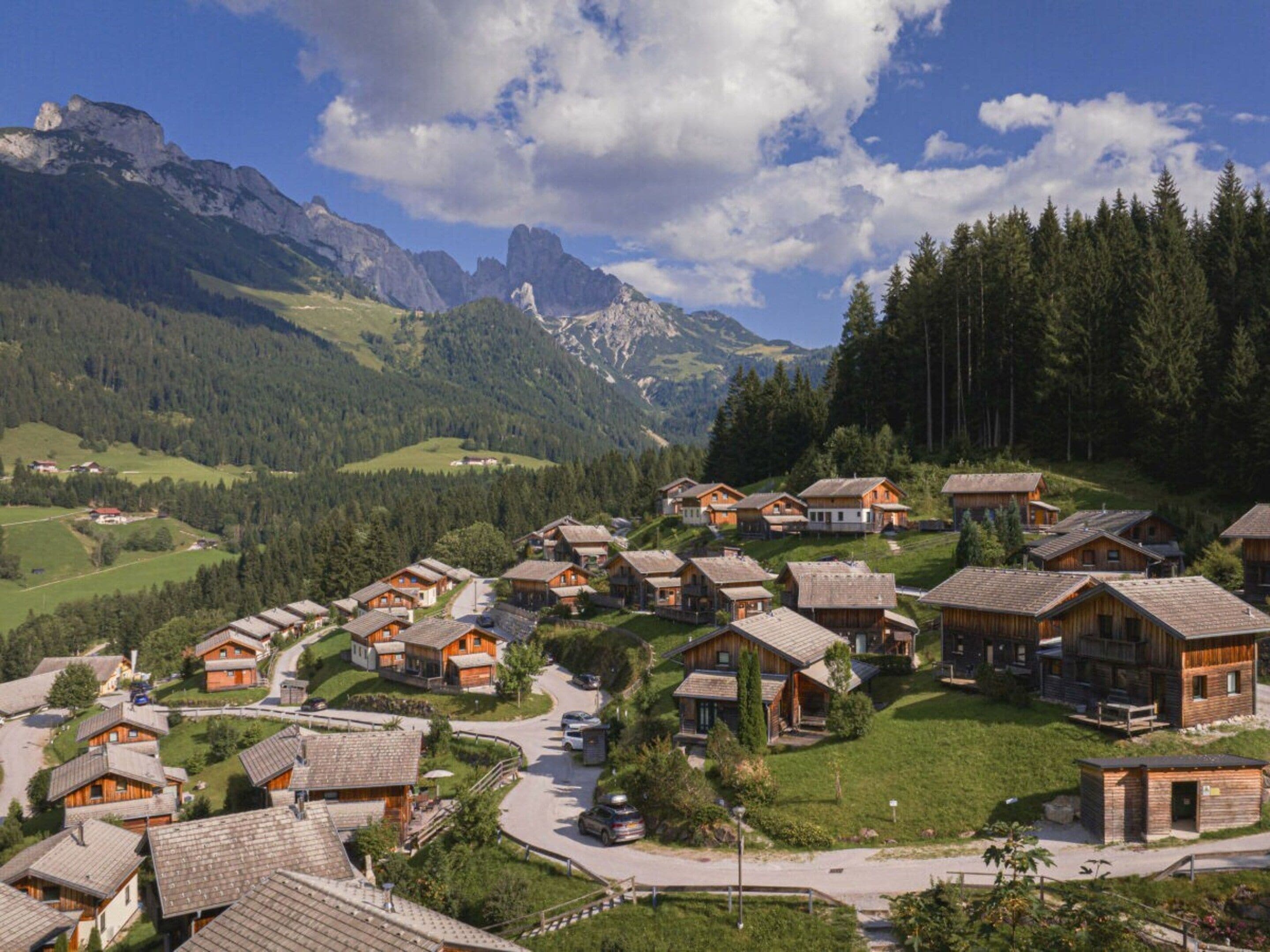A cluster of wooden chalets with a mountain backdrop, a winding road, and a clear sky.