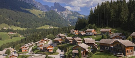 A cluster of wooden chalets with a mountain backdrop, a winding road, and a clear sky.