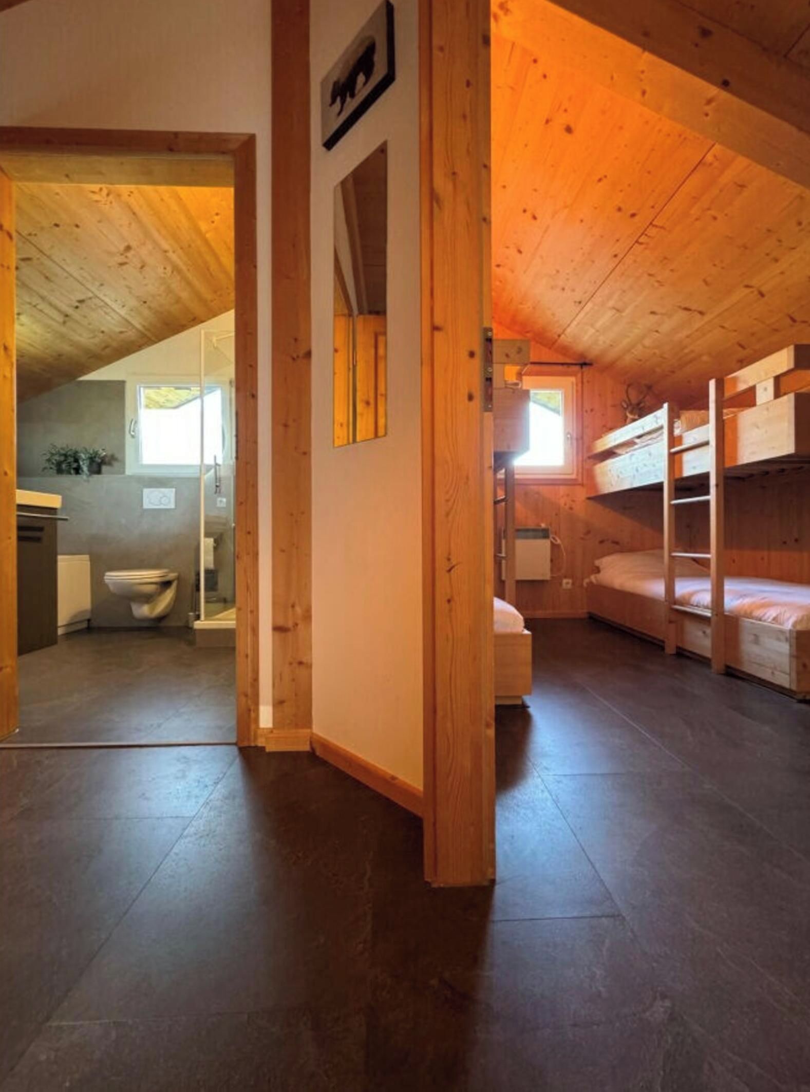 Un intérieur en bois avec des lits superposés, une salle de bain et une porte visible donnant sur une autre pièce.