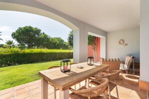 Een terras buiten met een houten tafel en rieten stoelen, een kandelaar van glas en een lantaarn.